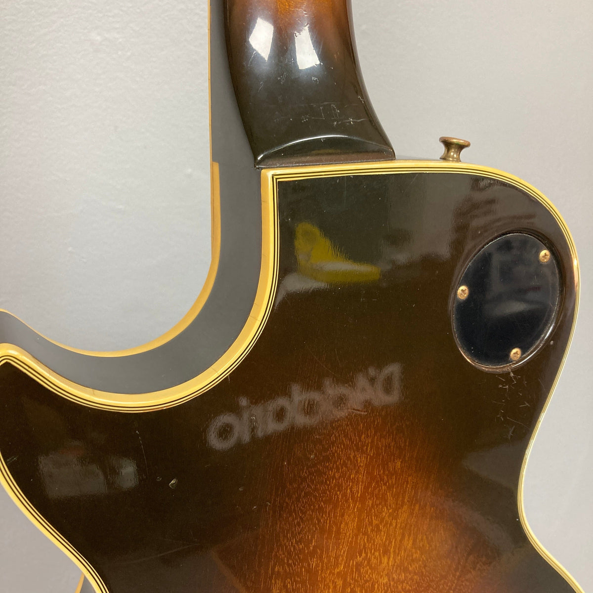 Close-up of a 1980 Gibson Les Paul Custom in Tobacco Sunburst, featuring the neck joint, black electronics cover, and cream binding, set against a gray wall.