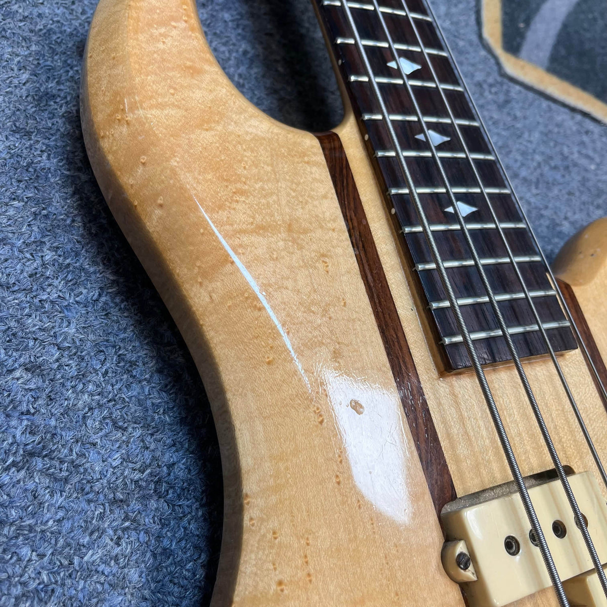Close-up of a 1982 B.C. Rich Eagle Bass—USA Made—showing its natural wood grain, neck-through body, decorative fretboard inlays, original electronics, and part of a pickup; a professionally set up vintage classic.