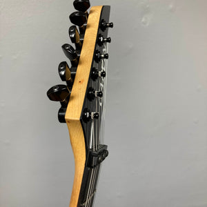 Close-up of a 1992 Carvin Ultra V USA headstock with six tuners and metal strings, featuring a Kahler Steeler Trem and MJ-wound Seymour Duncan DCJ, set against a plain light-colored wall.