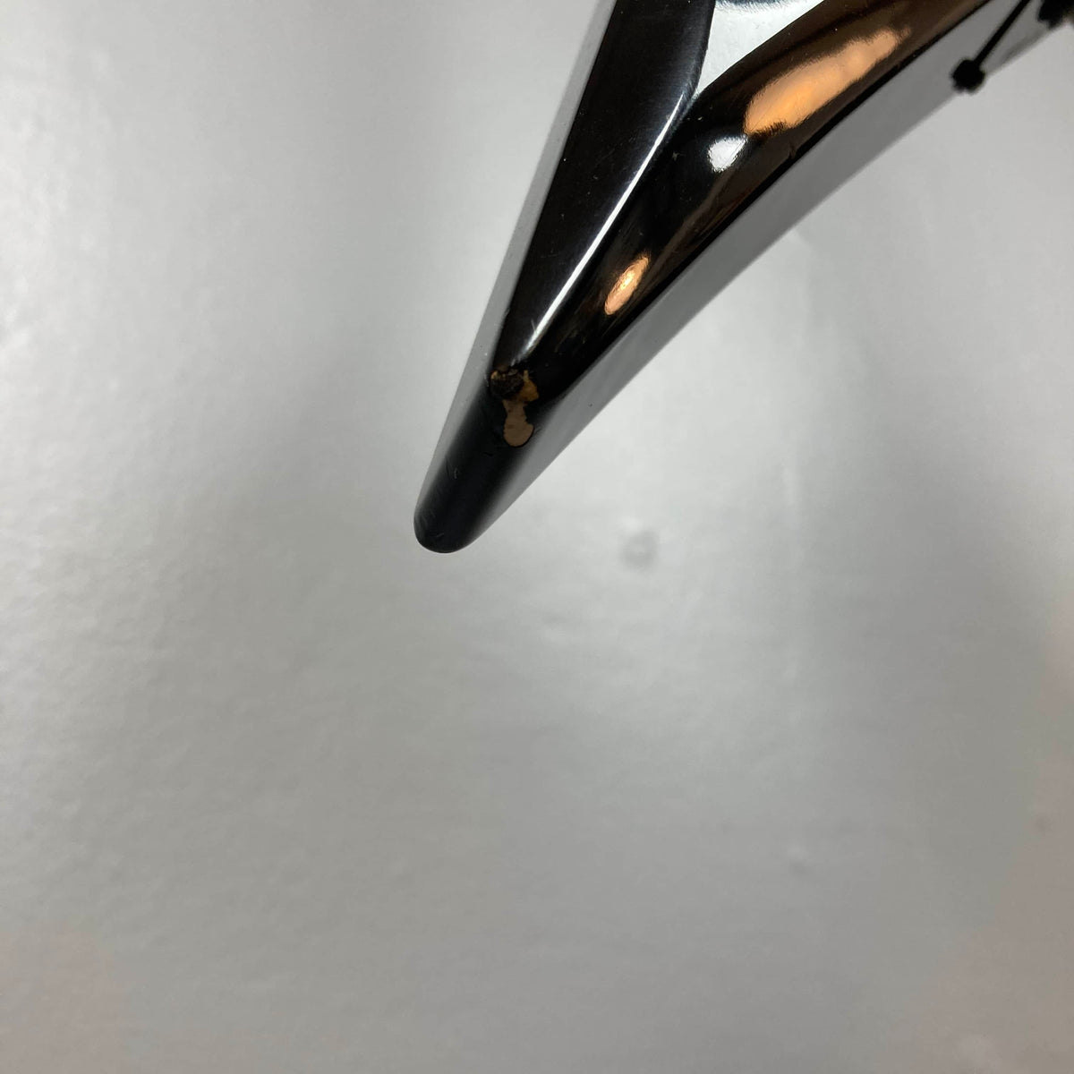 Close-up of the tip of a 1992 Carvin Ultra V USA – Kahler Steeler Trem, MJ-Wound Seymour Duncan DCJ guitar with a small chipped area showing a lighter color underneath, set against a plain white background.
