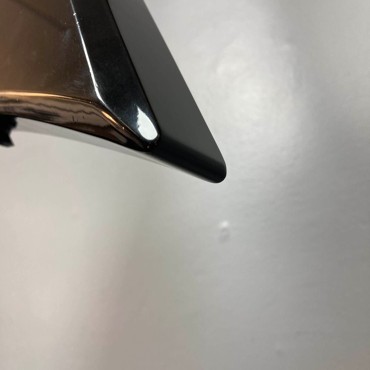 Close-up of the shiny black tip of a metallic object, likely from a Carvin 1992 Ultra V USA with Kahler Steeler Trem and MJ-wound Seymour Duncan DCJ, set against a plain light gray background.