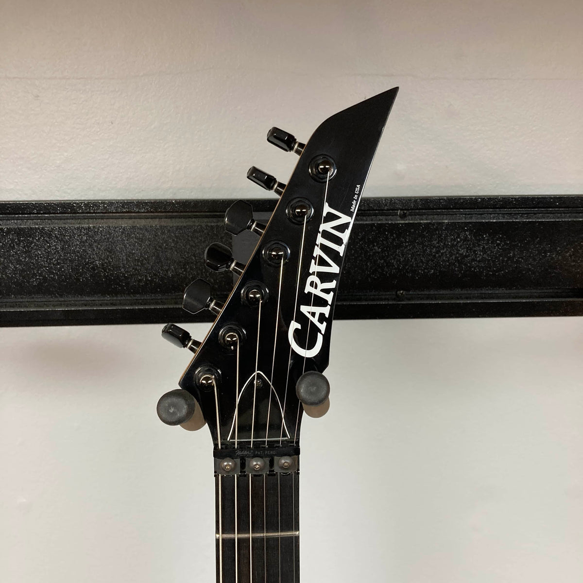 Headstock of a Carvin 1992 Ultra V USA with six tuners, black hardware, Kahler Steeler Trem, MJ‑wound Seymour Duncan DCJ pickup, and logo, shown against a white wall with a black horizontal bar.