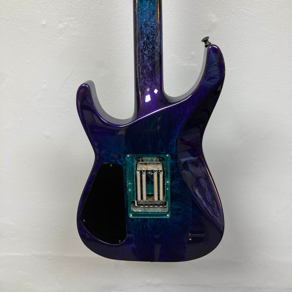 Rear view of a 1995 Jackson SL1 Soloist Custom Shop Eerie Dess Swirl electric guitar, featuring a glossy blue and purple marbled finish, exposed electronics cavity with no back cover plate, made by Jackson’s USA Custom Shop, and positioned against a plain white wall.