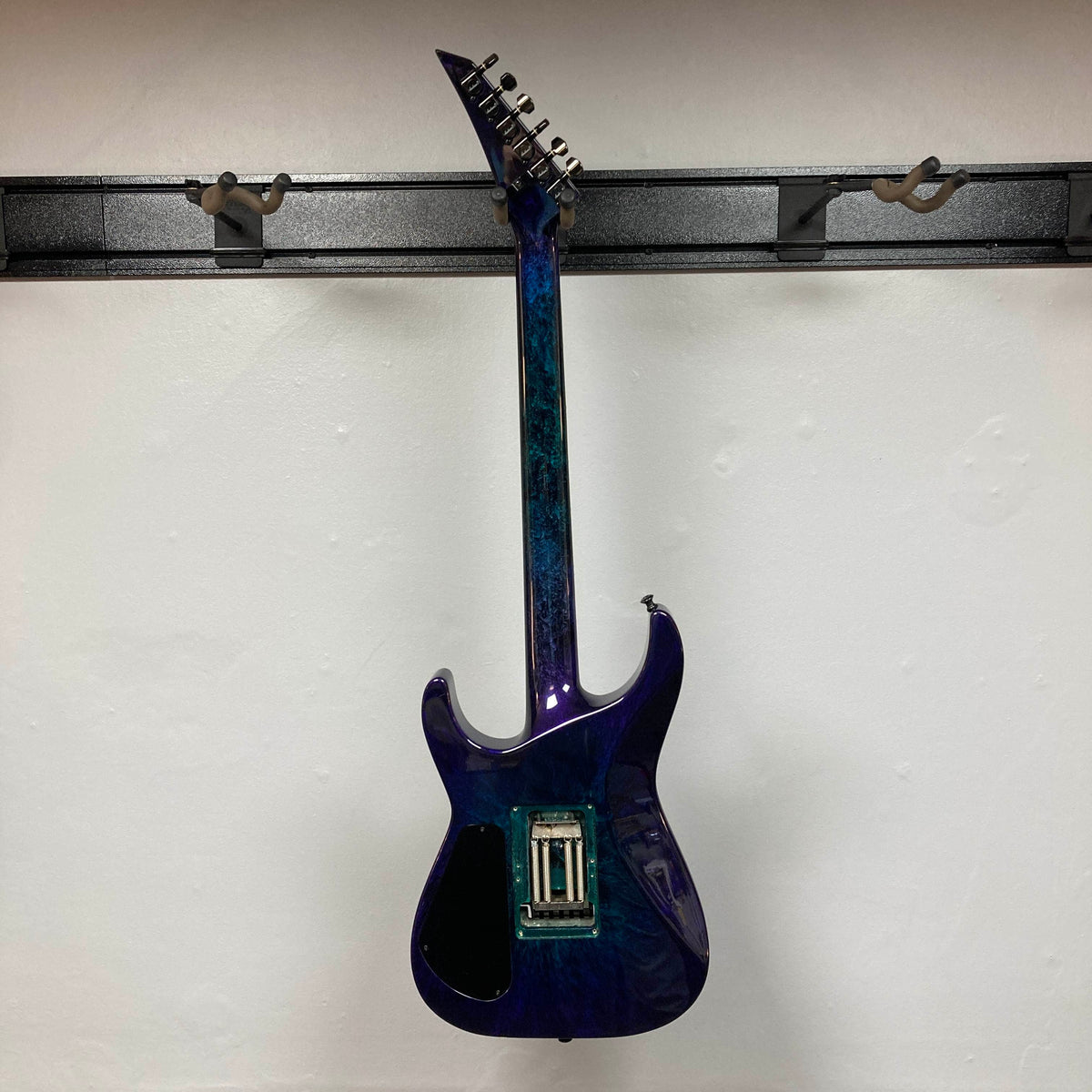 A 1995 Jackson SL1 Soloist Custom Shop electric guitar in Eerie Dess Swirl finish, currently without strings or pickups, is displayed on a black wall mount against a white background, highlighting its premium craftsmanship from Jackson’s USA Custom Shop.