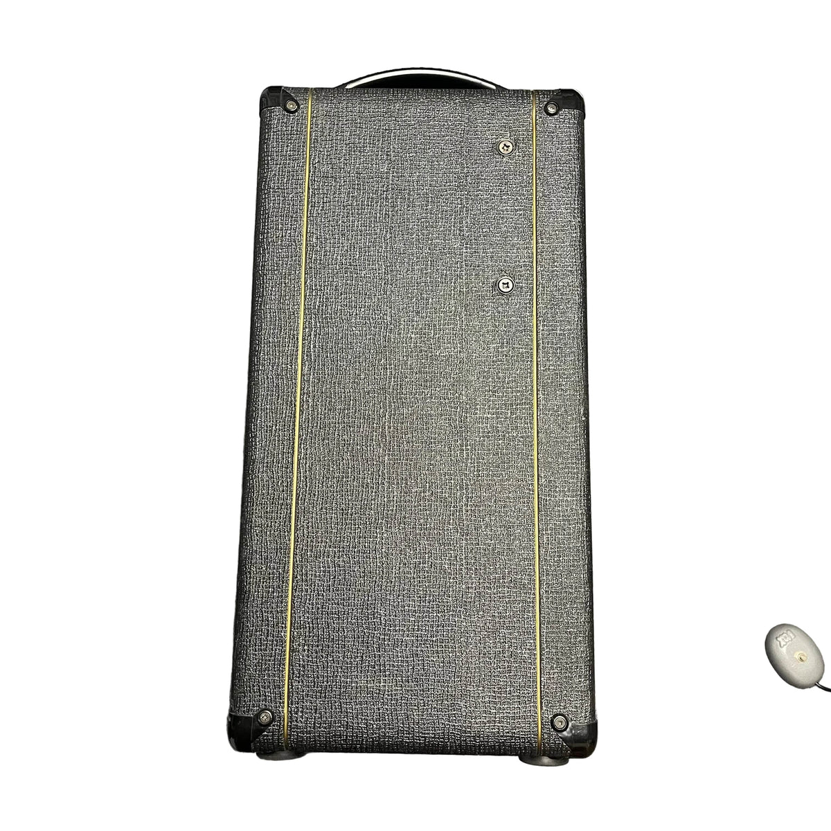 A rectangular, black textured Vox speaker cabinet with yellow lines stands upright; a small white wireless earbud rests in the corner, evoking the classic 2004 Vox AC30/6TB made in England with Celestion Alnico Blues.