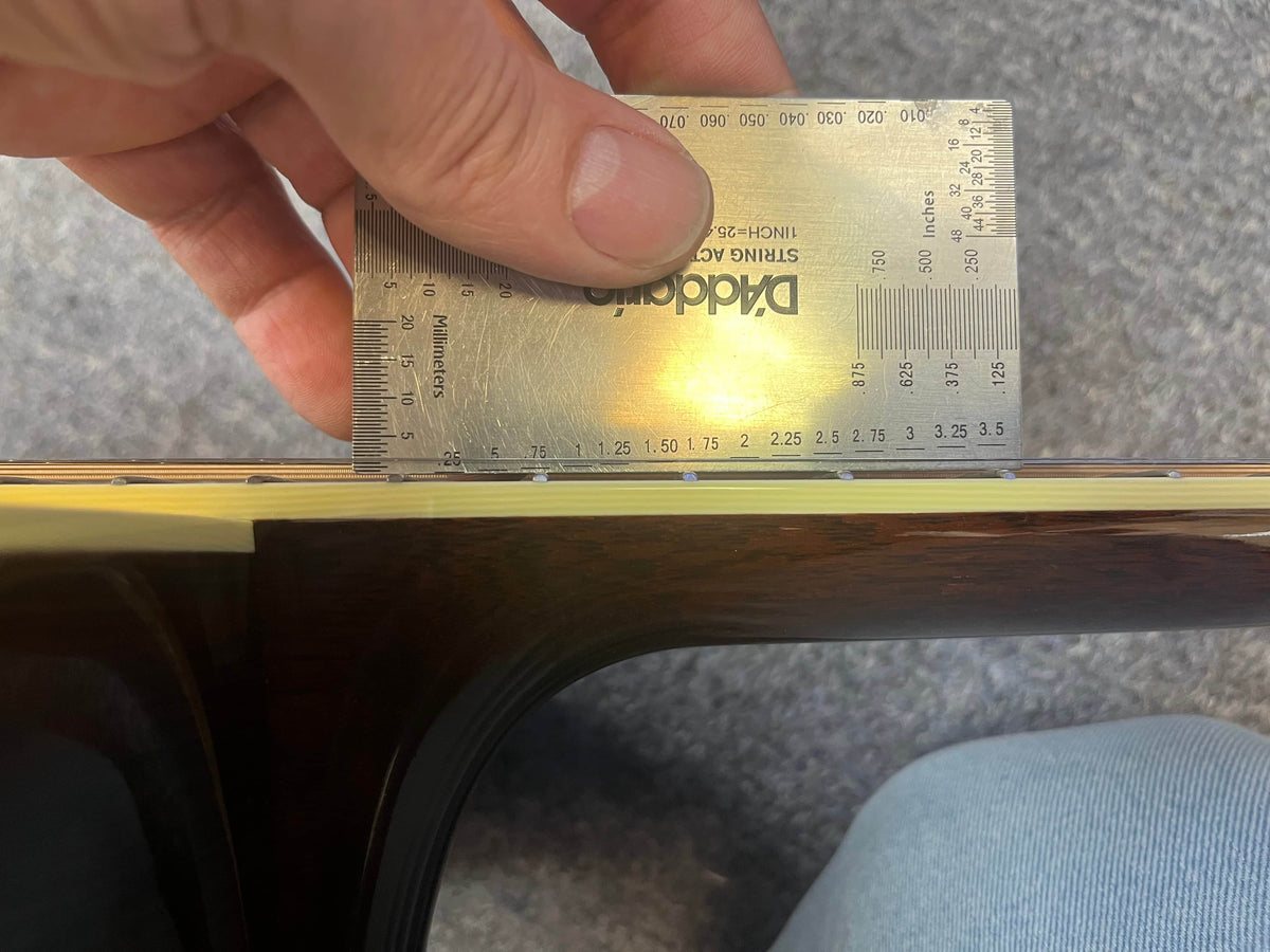 A metal ruler measures the string height above the fretboard of this 2005 Collings CJ BaA, a fine Brazilian Rosewood & Adirondack Spruce guitar by Collings.