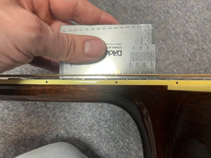 A hand uses a metal ruler to measure string height above the fretboard on a Collings 2005 CJ BaA acoustic guitar with Brazilian rosewood back and sides and an Adirondack spruce top.