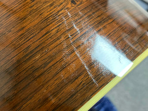 Close-up of a wooden surface with scratches and a reflective patch, likely part of a 2005 Collings CJ BaA guitar made from Brazilian Rosewood and Adirondack Spruce by Collings.