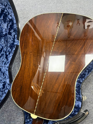 The back of a 2005 Collings CJ BaA—Brazilian Rosewood & Adirondack Spruce—guitar by Collings, featuring a glossy wood finish, center inlay, and cream binding, resting in a blue velvet-lined case.