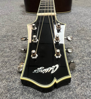 Close-up of a black headstock with six tuning pegs and cream binding, branded "Collings," from the 2005 Collings CJ BaA—Brazilian Rosewood & Adirondack Spruce—resting elegantly on a gray carpet.
