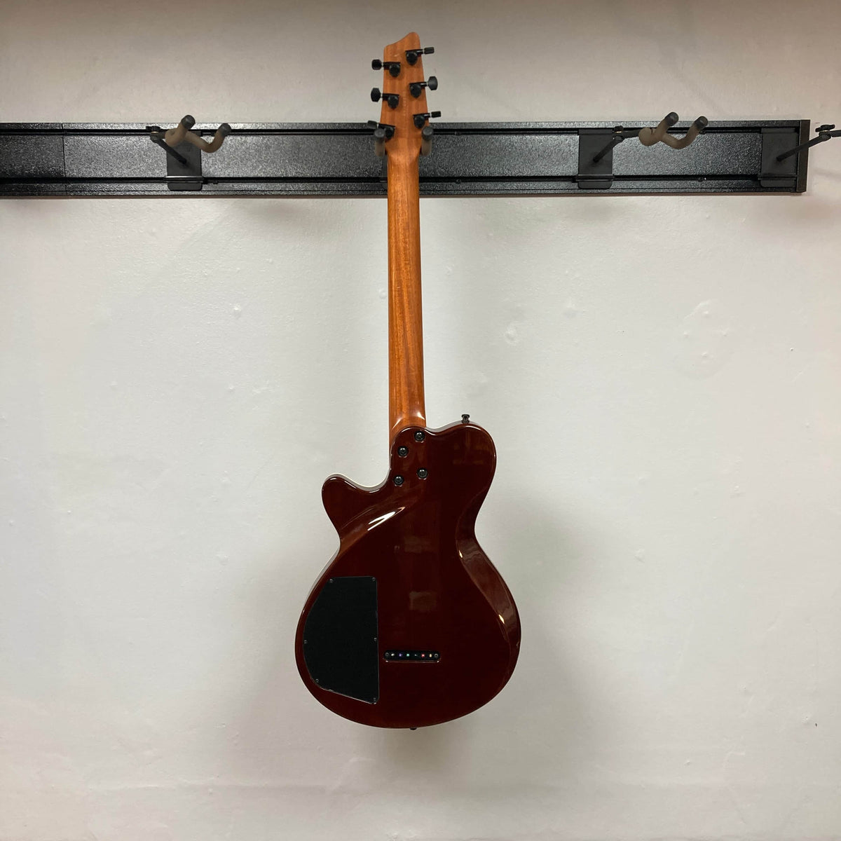 A 2009 Godin Summit CT electric guitar with a carved flame maple cap hangs on a wall-mounted rack, displayed with its back facing forward.
