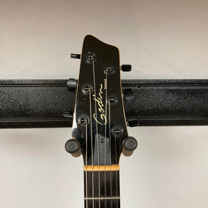 Headstock of a 2009 Godin Summit CT with six tuning pegs, mounted on a black wall hanger against a light wall—an ideal display piece for fans of flame maple Godin electric guitars.