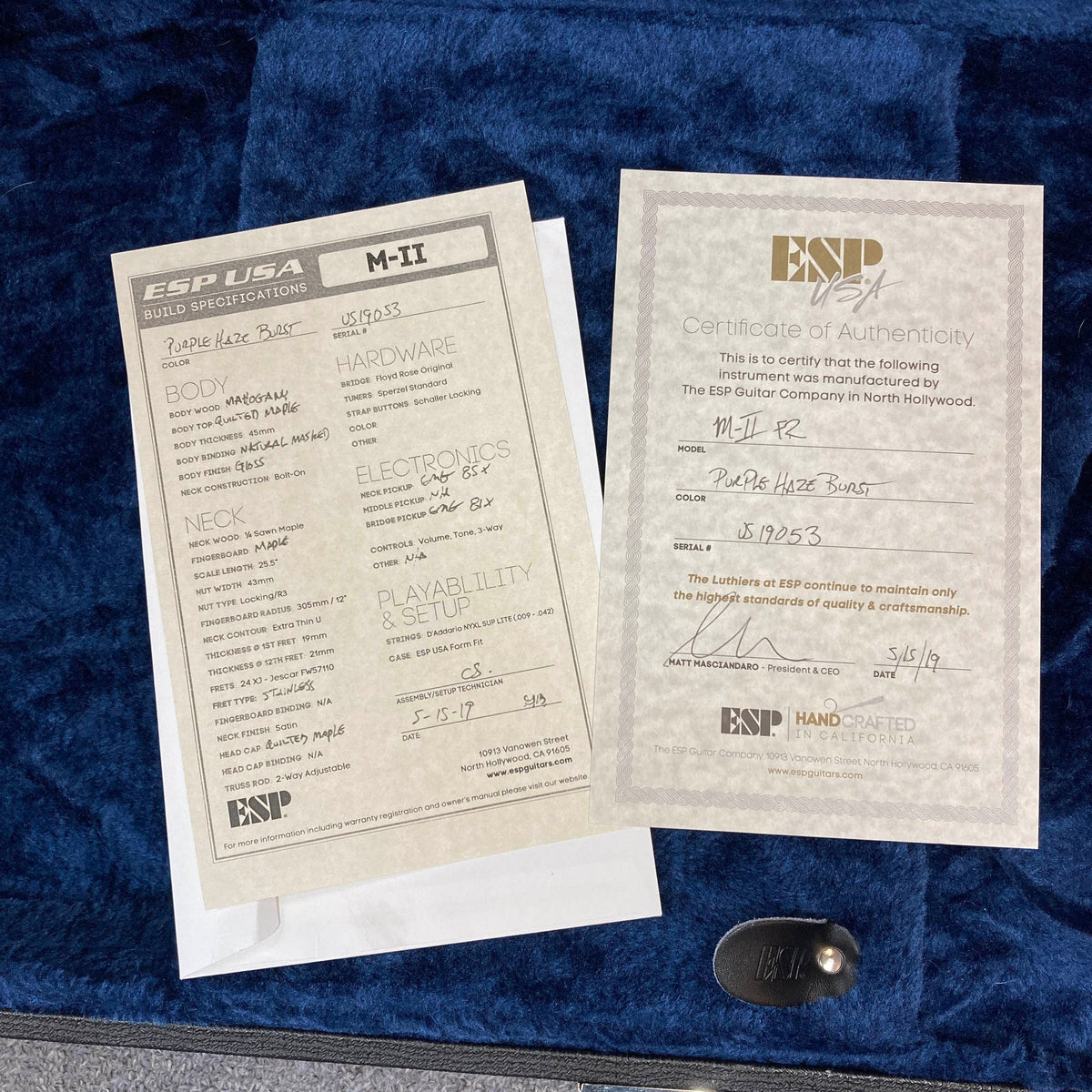 Two ESP specification and warranty cards, one of which features handwritten details, rest atop a blue velvet-lined surface—the perfect accompaniment to your American-made electric guitar, like the striking 2019 ESP USA M-II Purple Haze Burst w/Case from ESP.