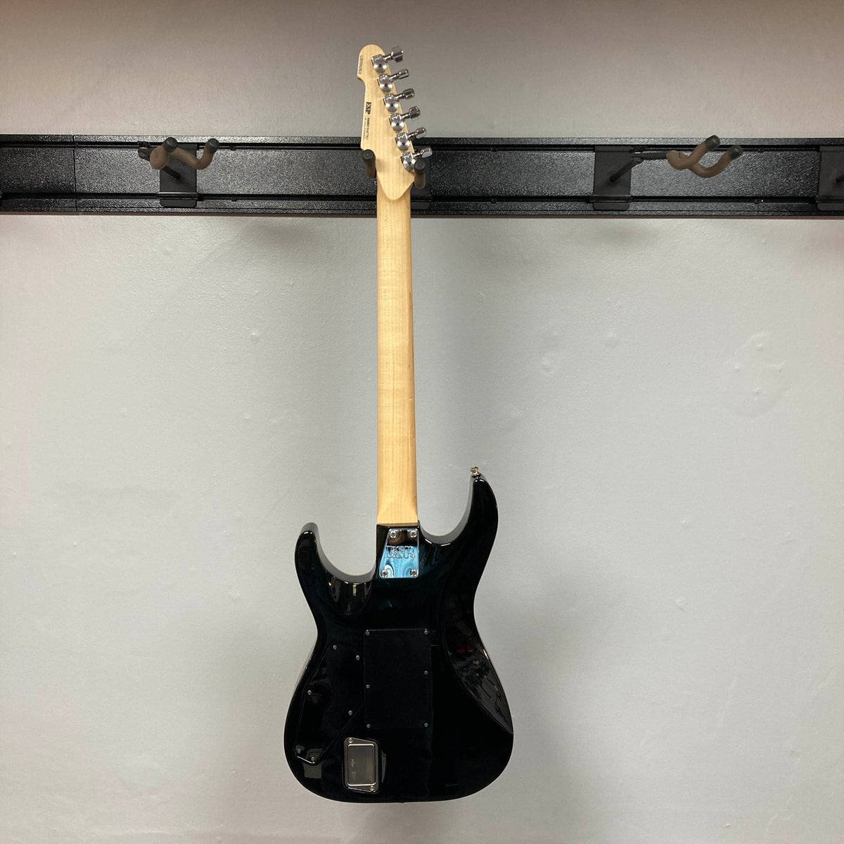 A 2019 ESP USA M-II in Purple Haze Burst, an American-made electric guitar by ESP, is hanging on a wall-mounted rack, shown from the back with the neck and tuning pegs visible.