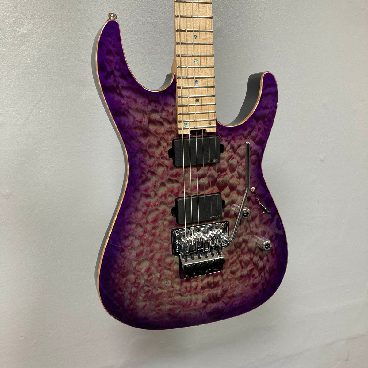 The ESP 2019 USA M-II Purple Haze Burst electric guitar features a breathtaking quilted maple top finished in Purple Haze Burst, a maple neck, dual humbucker pickups, and a Floyd Rose tremolo system. This American-made ESP model is shown photographed against a plain light-colored wall and comes complete with its case.