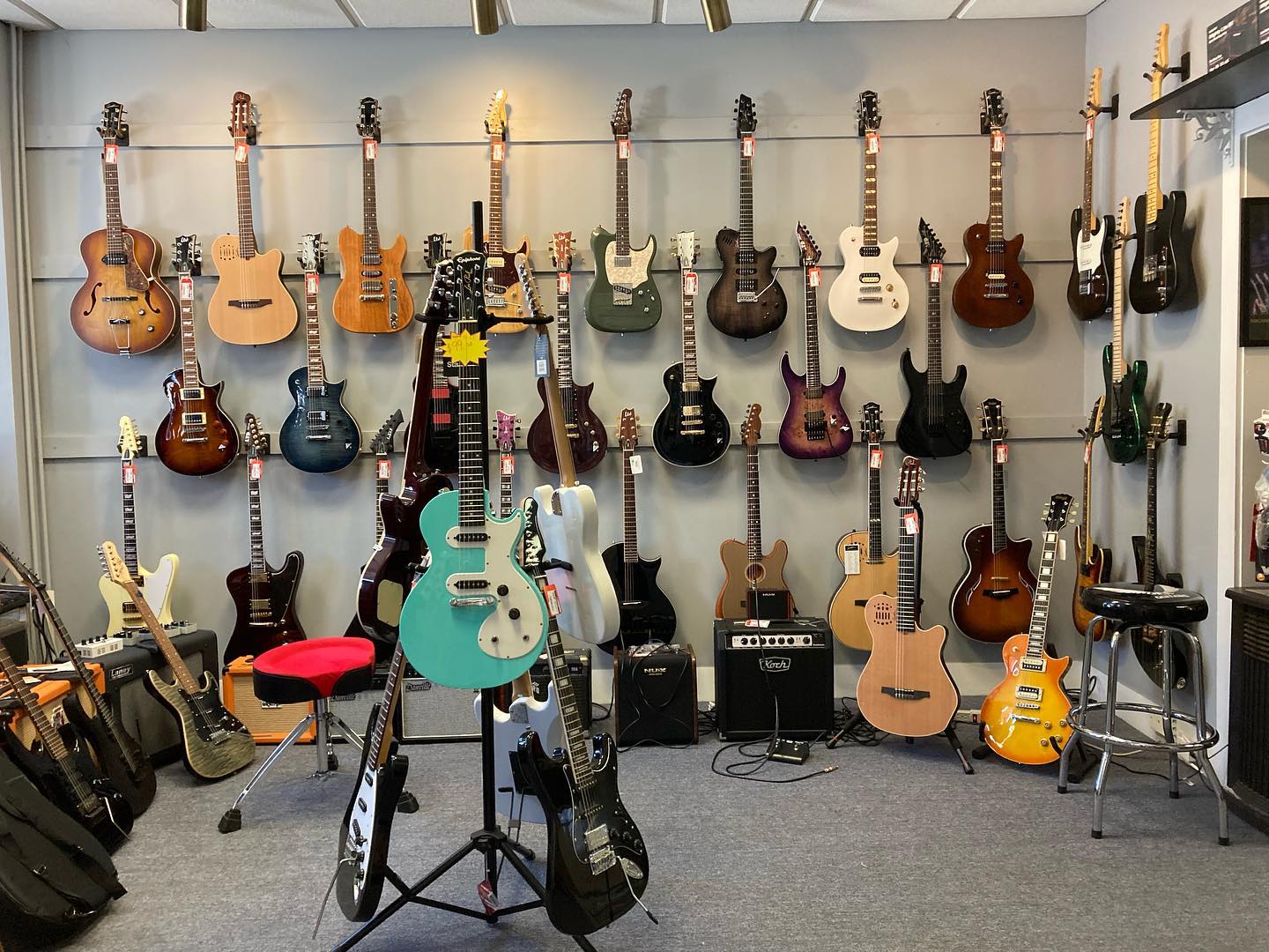 Guitar showroom featuring many brands hanging on walls and on floor stands.