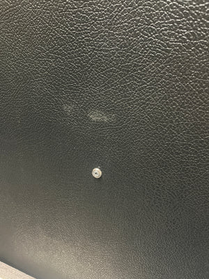 Close-up of a black textured surface—evocative of a vintage Marshall 1969 4x12 Cabinet with matching Celestion T1281 Greenbacks—featuring a small metal screw in the center and a faint smudge above it.