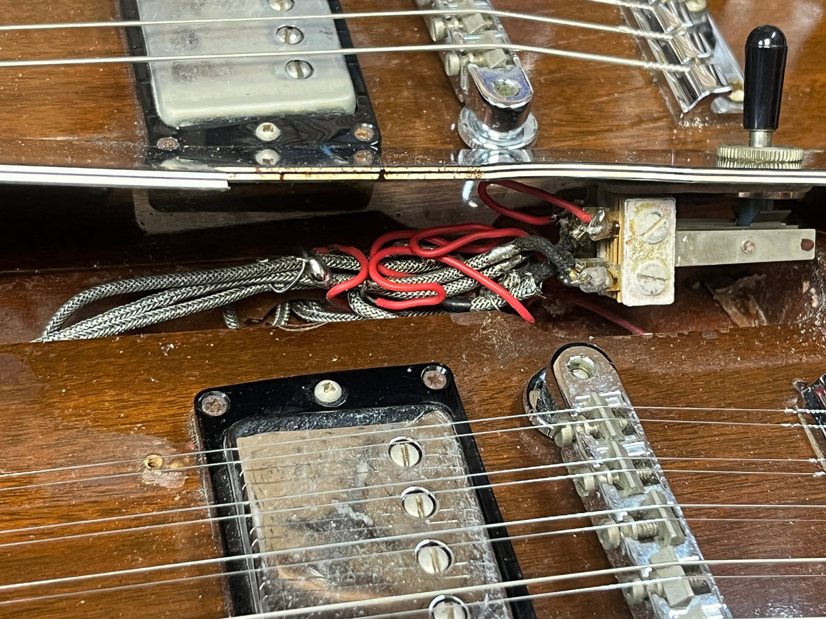 Close-up of a Gibson 1978 EDS-1275 Double Neck Walnut electric guitar, featuring exposed wiring, pickups, and the bridge area on its wooden body with visible dust and signs of wear—capturing the character of a well-used vintage instrument.