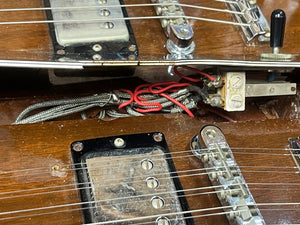 Close-up of a Gibson 1978 EDS-1275 Double Neck Walnut electric guitar, featuring exposed wiring, pickups, and the bridge area on its wooden body with visible dust and signs of wear—capturing the character of a well-used vintage instrument.