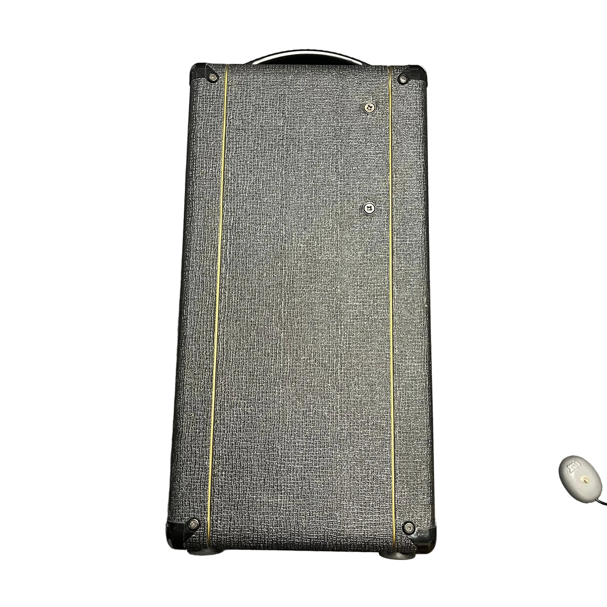 A rectangular, black textured Vox speaker cabinet with yellow lines stands upright; a small white wireless earbud rests in the corner, evoking the classic 2004 Vox AC30/6TB made in England with Celestion Alnico Blues.