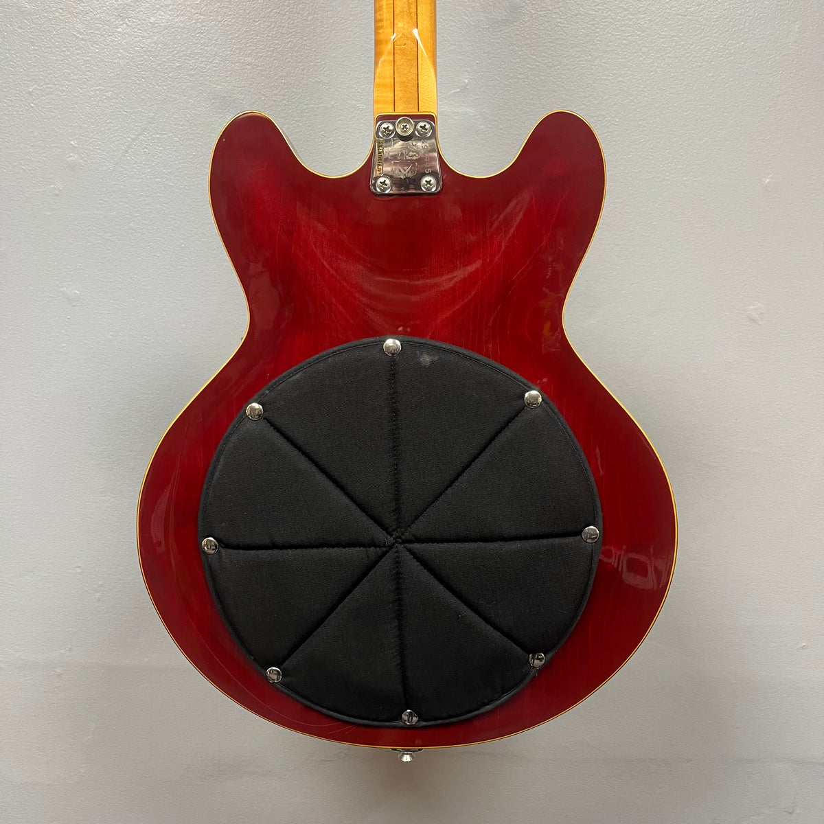 The back of a cherry 1967-68 Vox Sidewinder IV Bass (V272) by Vox features a large, black, padded circular attachment covering the semi-hollow body.