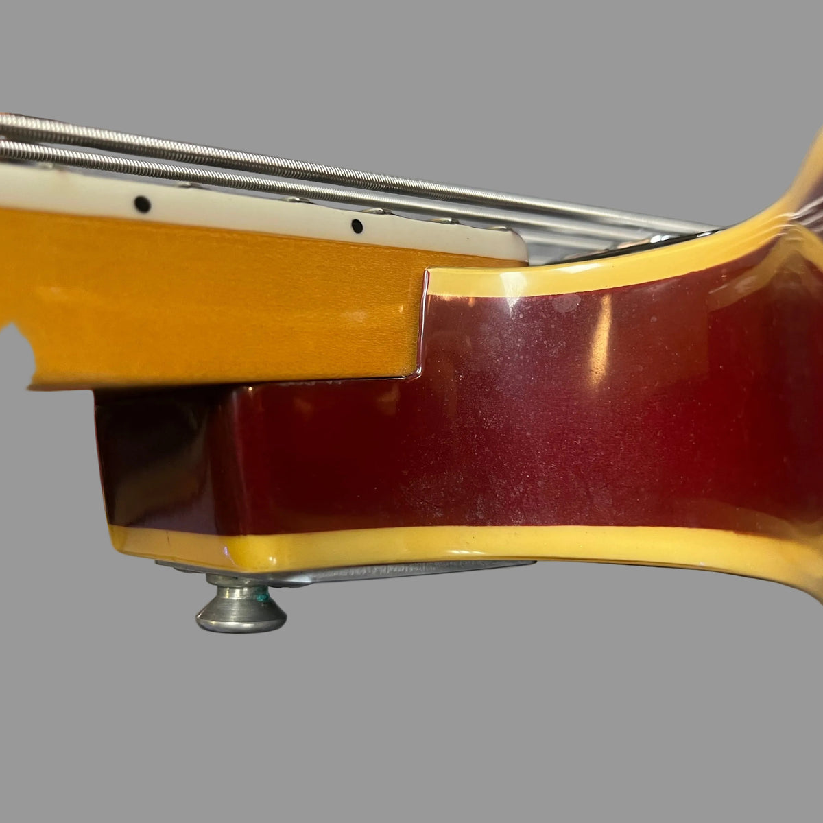 Close-up of the neck joint and body of a 1967-68 Vox Sidewinder IV Bass (V272) Cherry by Vox, featuring metal strings and a glossy cherry red finish, set against a plain gray background.