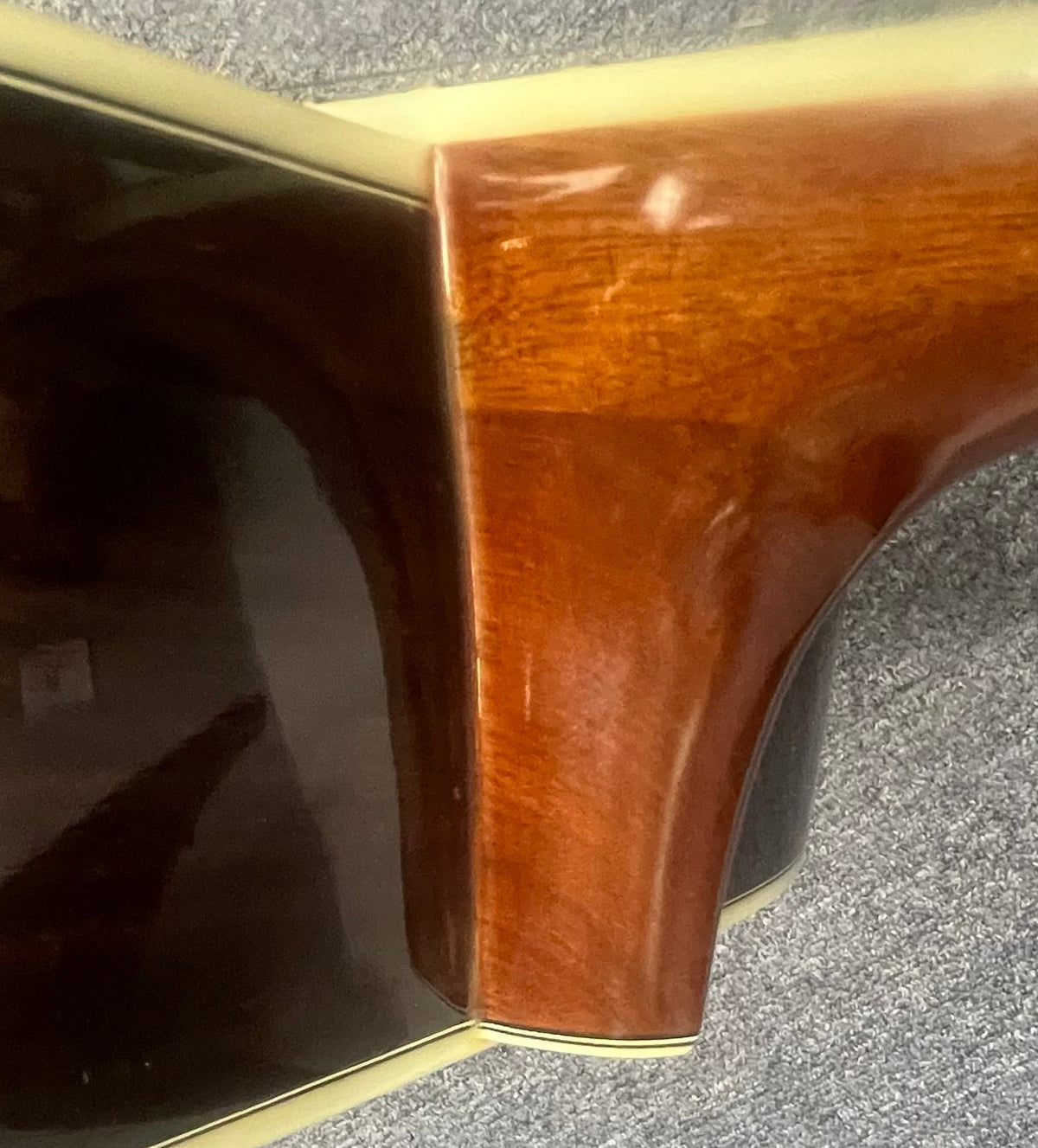 Close-up of the neck joint on a vintage Sigma DR-35 acoustic guitar (Made in Japan), highlighting its glossy wood finish and cream binding, shown resting on a gray carpet.