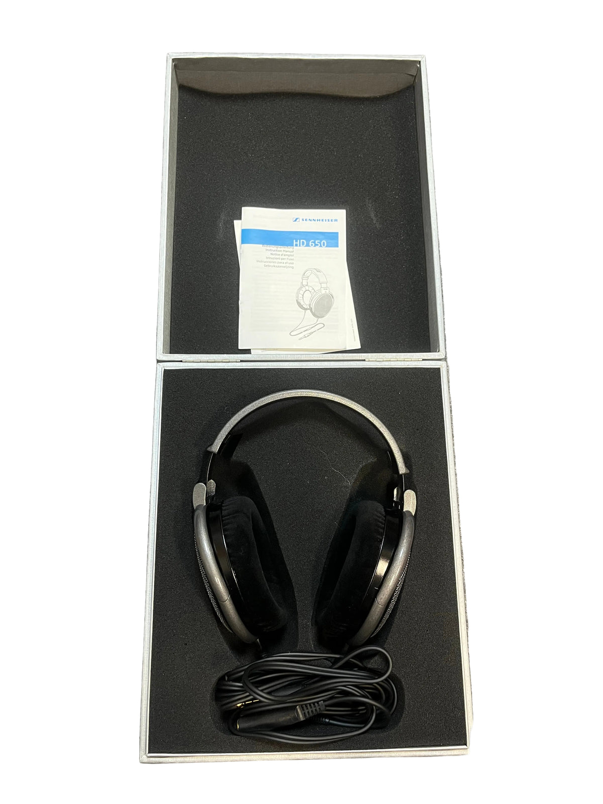 A pair of preowned Sennheiser HD 650 Reference Class open-back headphones, featuring a coiled cable and instruction manual, are neatly arranged inside an open, foam-padded box—making them an ideal option for any audiophile.