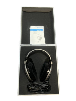 A pair of preowned Sennheiser HD 650 Reference Class open-back headphones, featuring a coiled cable and instruction manual, are neatly arranged inside an open, foam-padded box—making them an ideal option for any audiophile.