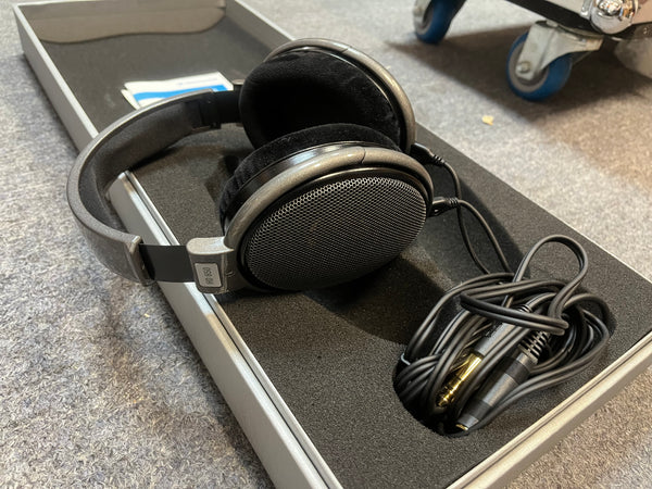 A pair of preowned Sennheiser HD 650 Reference Class open-back headphones, featuring a coiled cable and instruction manual, are neatly arranged inside an open, foam-padded box—making them an ideal option for any audiophile.