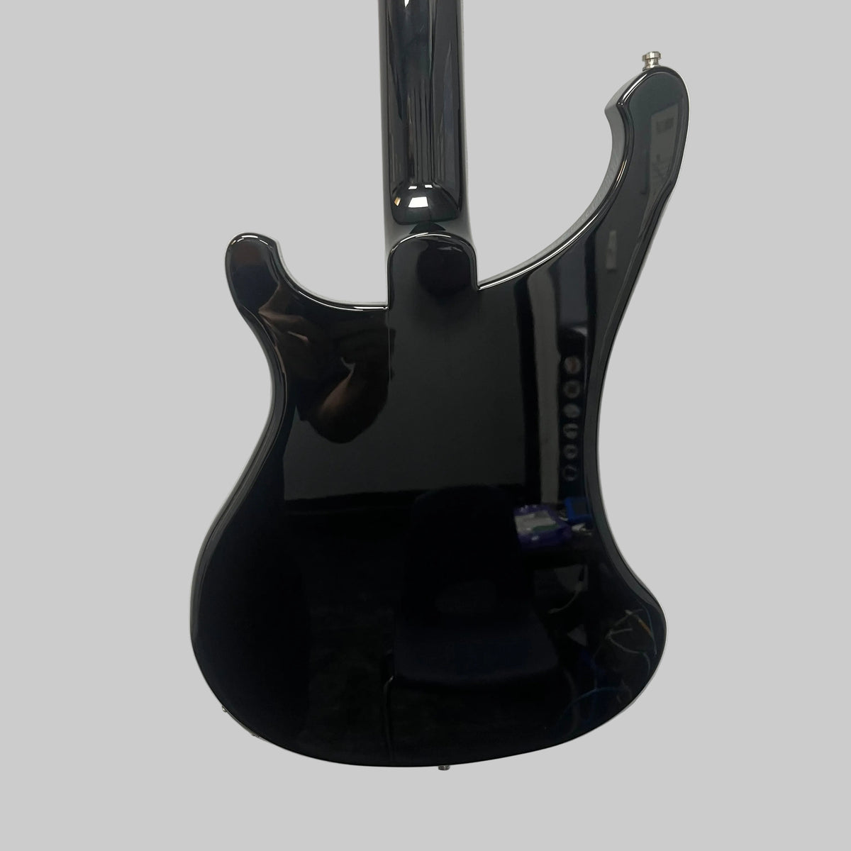 Mounted on a white wall, the sleek black Rickenbacker 4003 Bass Guitar – 2020 Jetglo w/Case reflects a person and objects in the room. Its lustrous finish and signature curves capture the timeless allure of this iconic Rickenbacker bass.