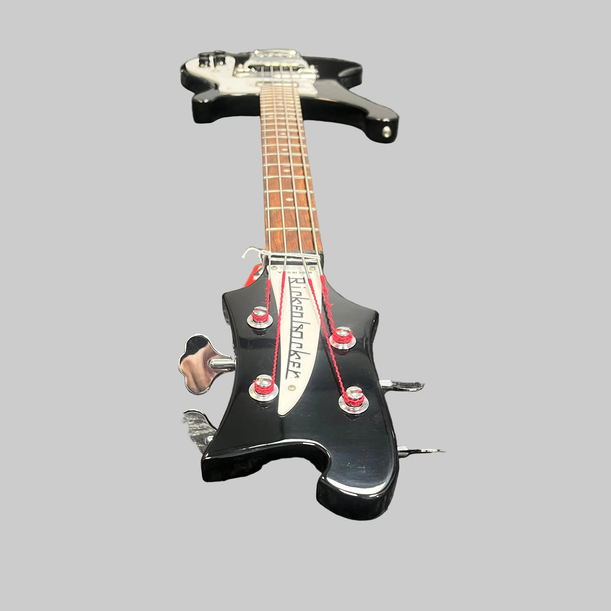 A Rickenbacker 4003 Bass Guitar – 2020 Jetglo w/Case featuring vivid red strings is lying flat on a grey background, viewed from the headstock end.