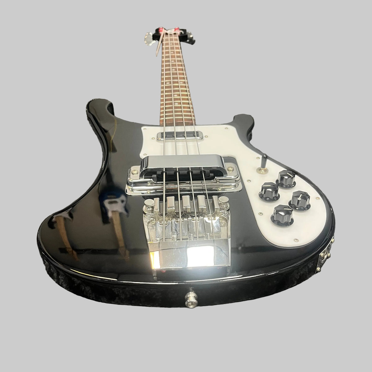 Rickenbacker 4003 Bass Guitar – 2020 Jetglo w/Case, featuring a sleek black finish with a white pickguard, four control knobs, and chrome bridge, photographed from a low angle against a plain gray background—a striking homage to the iconic Rickenbacker design.