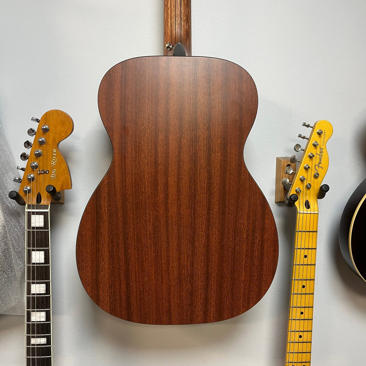 Back view of a Martin 00X1AE Acoustic-Electric Guitar mounted on a wall between two electric guitar headstocks.
