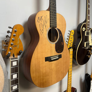 Martin 00X1AE Acoustic-Electric Guitar signed by Richie Kotzen, hanging on a wall between two electric guitars.