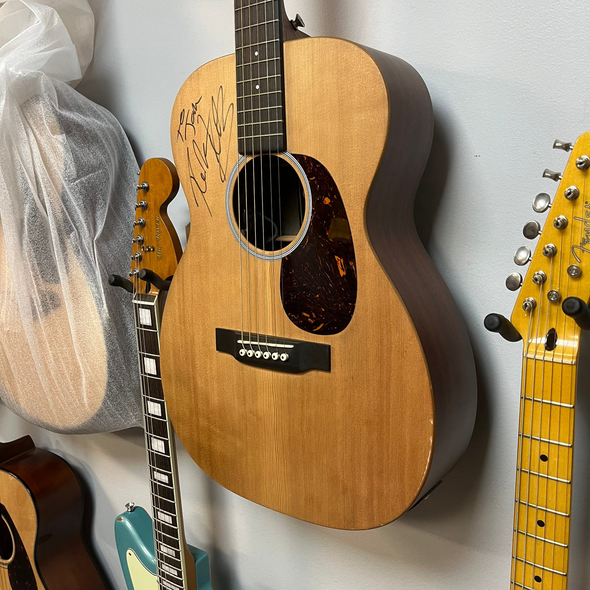 Martin 00X1AE Acoustic-Electric Guitar | Signed by Ex-Poison Guitarist Richie Kotzen hanging on a wall, featuring the autograph on the body above the soundhole.