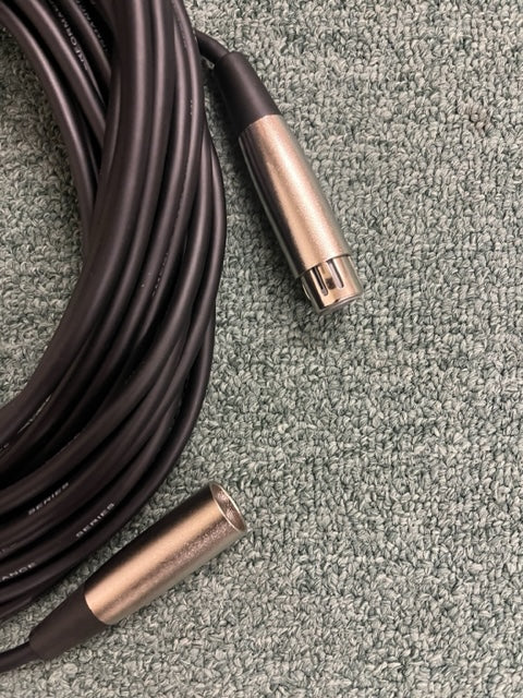 A coiled black American DJ MC-50 50ft XLR Microphone Cable with metal connectors lies on a textured gray carpet.