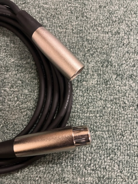 A coiled black American DJ MC-10 10ft XLR Microphone Cable with silver connectors rests on a textured light green surface—perfect for American DJ audio setups.