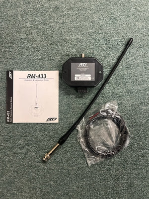 A Remote Technologies Inc (RTI) RM-433 433MHz RF Receiver Module, antenna, coiled cable in plastic, and operation manual for RTI control systems are shown on a green carpeted surface.