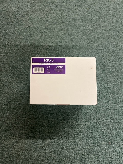 A white rectangular RTI RK-3 In-Wall Universal Controller by Remote Technologies Inc sits on green carpet, perfect as a home automation in-wall controller.