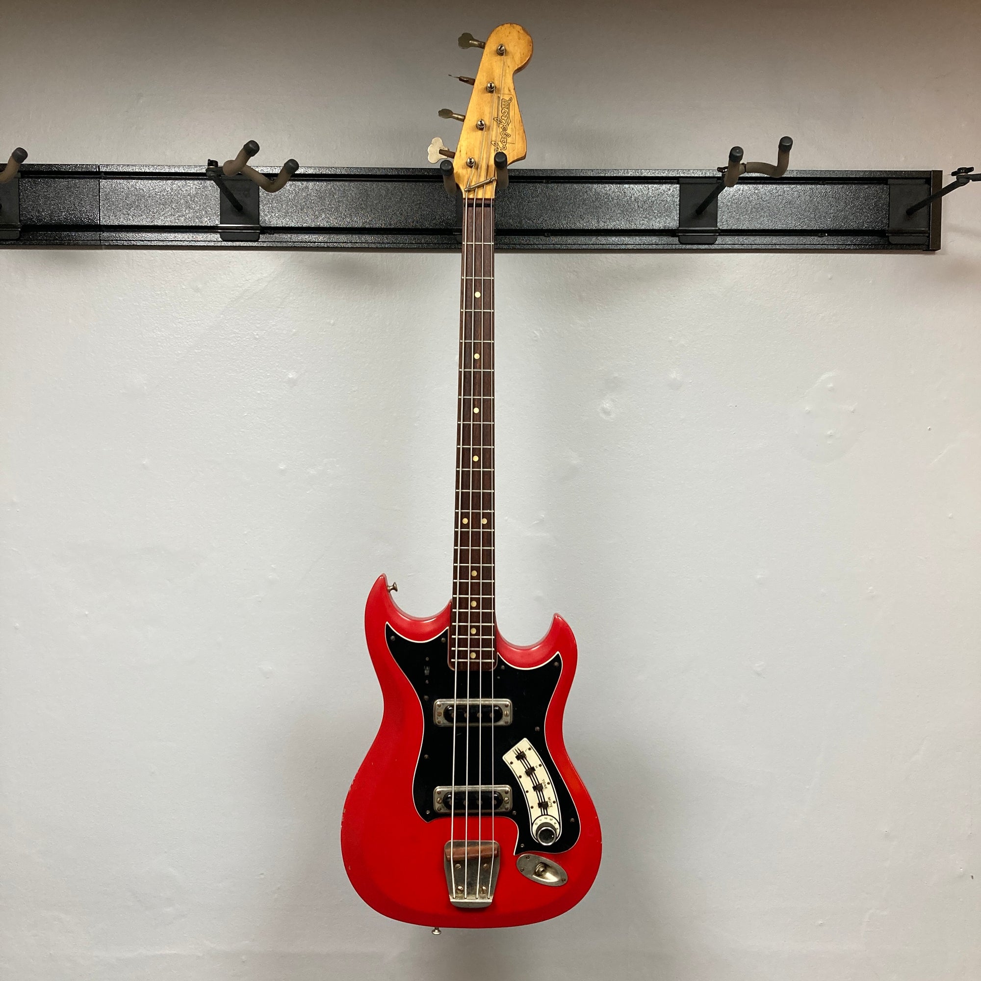 Hagstrom HII-B Mid-1960s Red Medium-Scale Bass, features dual pickups, distinctive design, vintage character, hanging against a light-gray wall.