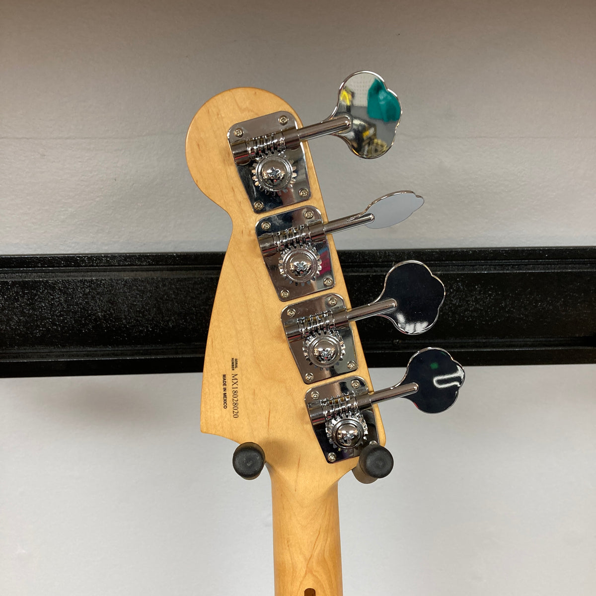 A Fender Mustang Player Bass PJ White Used with four metal tuning pegs on the headstock is displayed on a black wall hanger against a Polar White wall.
