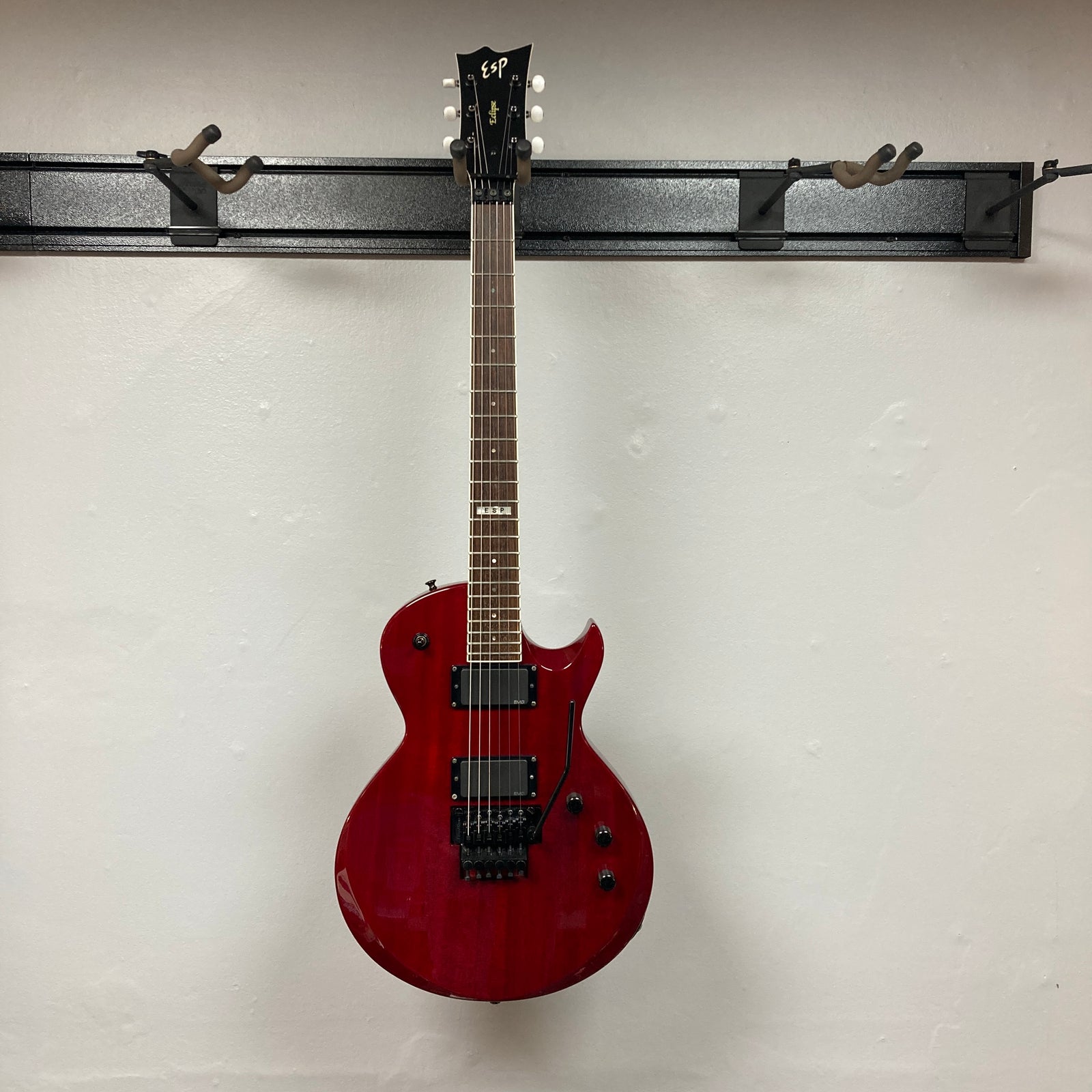 An ESP Standard Eclipse Transparent Cherry Red electric guitar with dual humbuckers, tremolo bridge, and four knobs is shown against a plain white wall. Includes case. Brand: Esp.