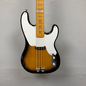 A close-up of the Fender Sting P Bass Sunburst by Fender, featuring a vintage-style sunburst finish, white pickguard, and maple neck, photographed against a plain gray wall.