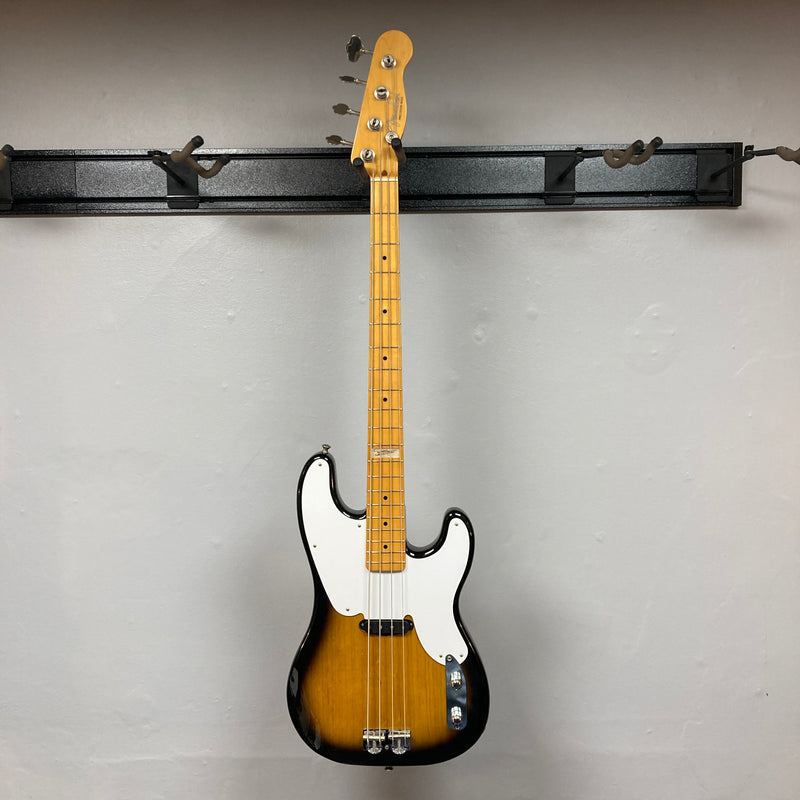 A close-up of the Fender Sting P Bass Sunburst by Fender, featuring a vintage-style sunburst finish, white pickguard, and maple neck, photographed against a plain gray wall.