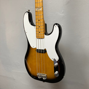 The Fender Sting P Bass Sunburst by Fender, featuring a white pickguard and maple neck, is photographed against a plain light gray wall, highlighting its classic vintage-style electric bass design.
