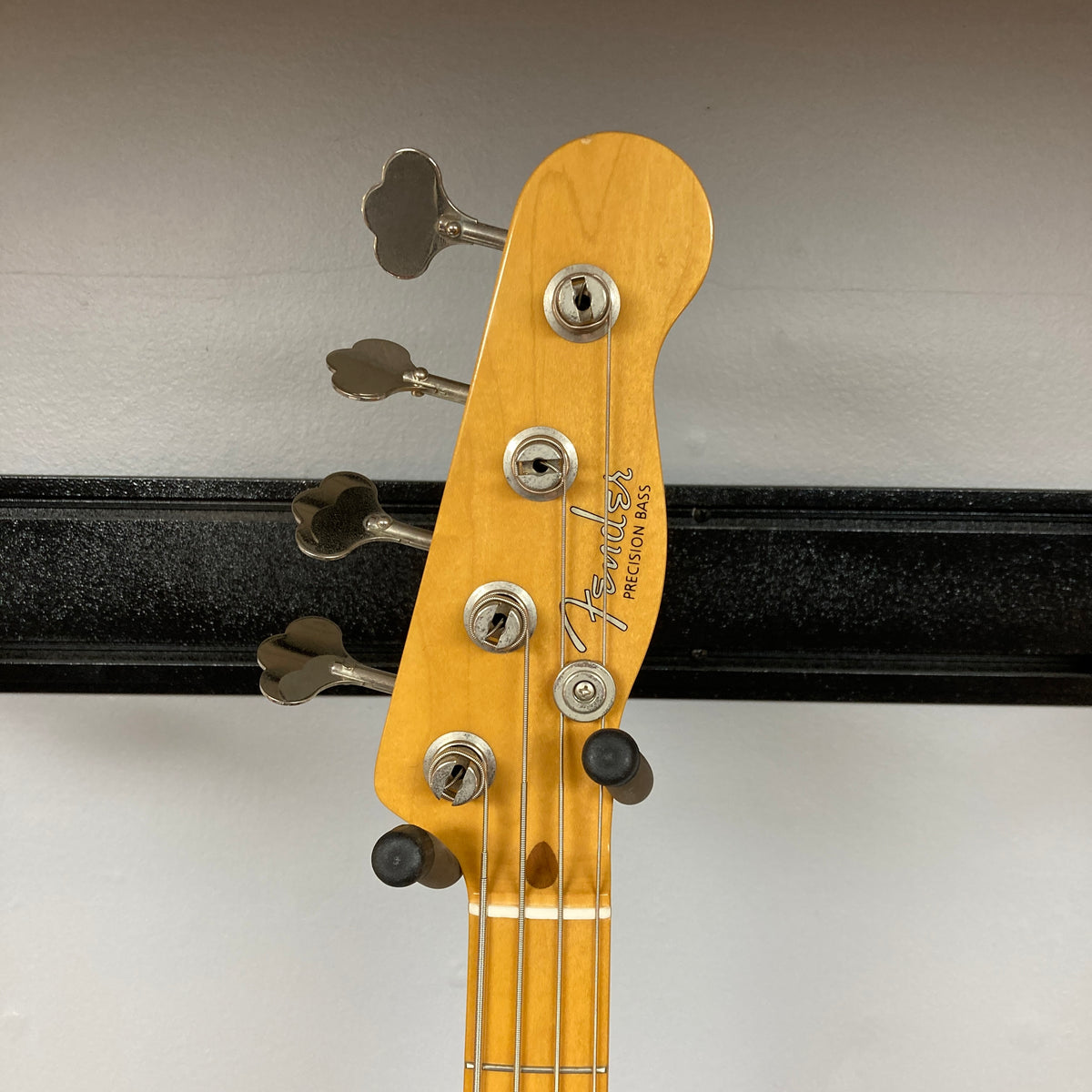 Close-up of the headstock of a Fender Sting P Bass Sunburst by Fender, showing four tuning pegs and black string retainers on a wall rack. This standout Made in Japan Precision Bass features a vintage-style design.