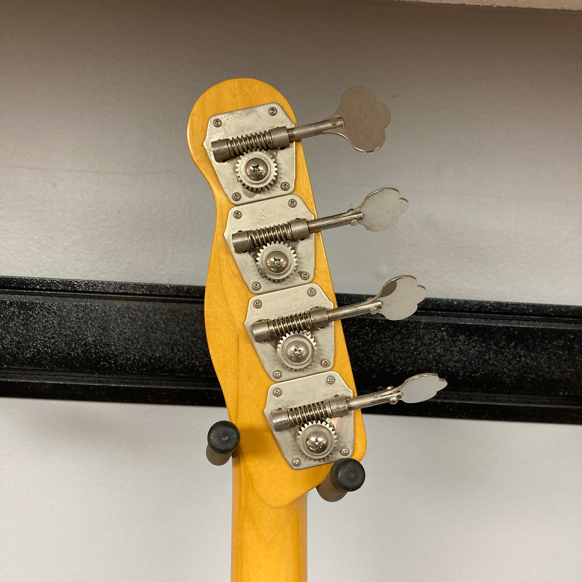 Close-up of the tuning pegs and headstock of the Fender Sting P Bass Sunburst by Fender, with its neck resting on a black guitar stand against a white wall.