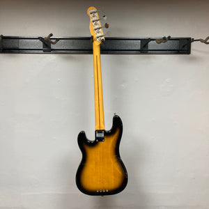 A Fender Sting P Bass Sunburst by Fender hangs from its neck on a black wall-mounted rack against a plain white wall.