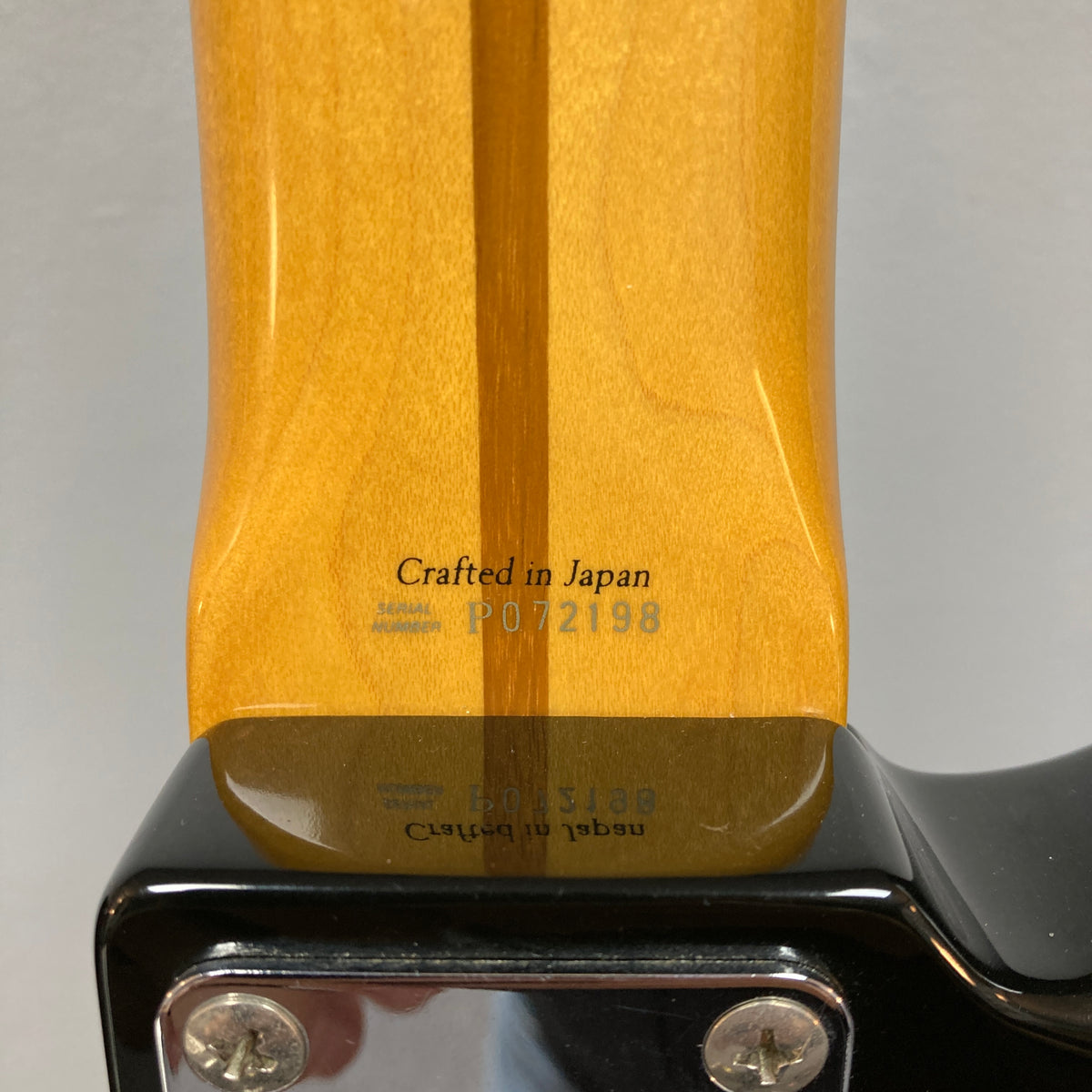 Close-up of the neck joint on a Fender Sting P Bass Sunburst by Fender, featuring "Crafted in Japan" and serial number "P072198" printed on the wood of this vintage-style electric bass.